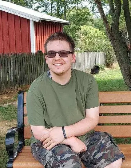 Zach smiling, sitting on a park bench.
