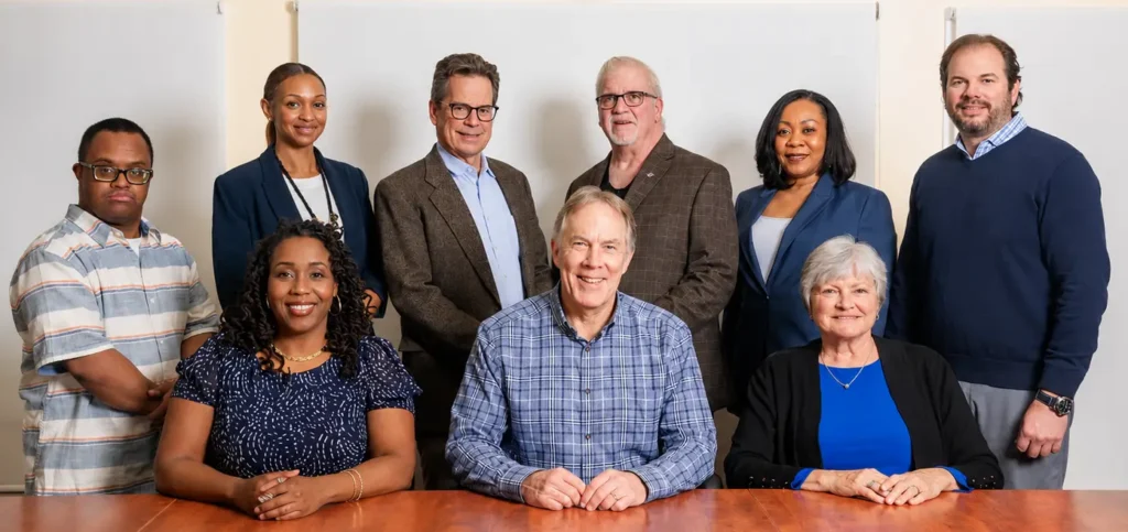 The Bello Machre Leadership Team gathered around a conference table for a group portrait, smiling and looking toward the camera.