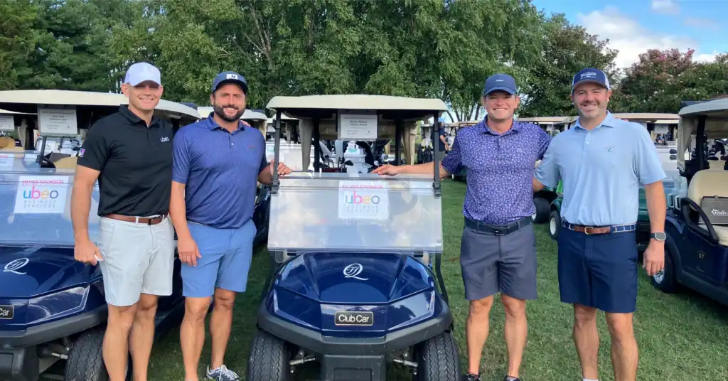 Team Ubeo posing by golf cart at golf event.